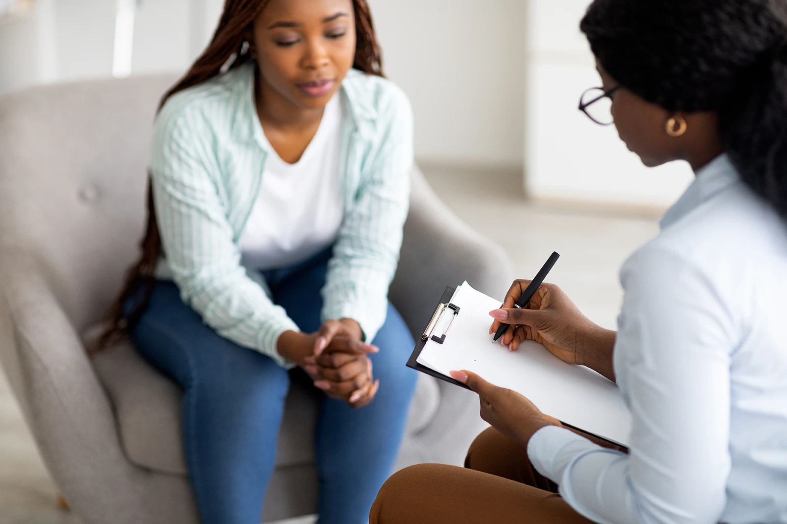 A Black therapist taking notes on a clipboard during a session with a client